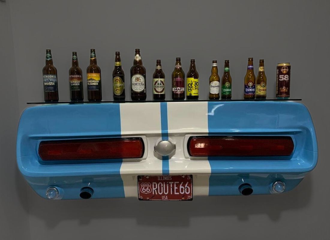 Bar criativo em fibra de vidro feito com a traseira azul de um carro clássico com faixas brancas, placa Route 66 e prateleira de vidro com garrafas de cerveja