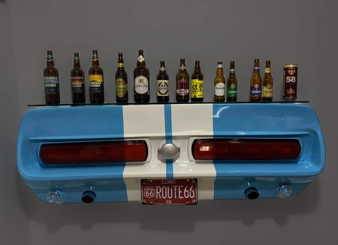 Bar criativo em fibra de vidro feito com a traseira azul de um carro clássico, placa Route 66 e prateleira de vidro com garrafas