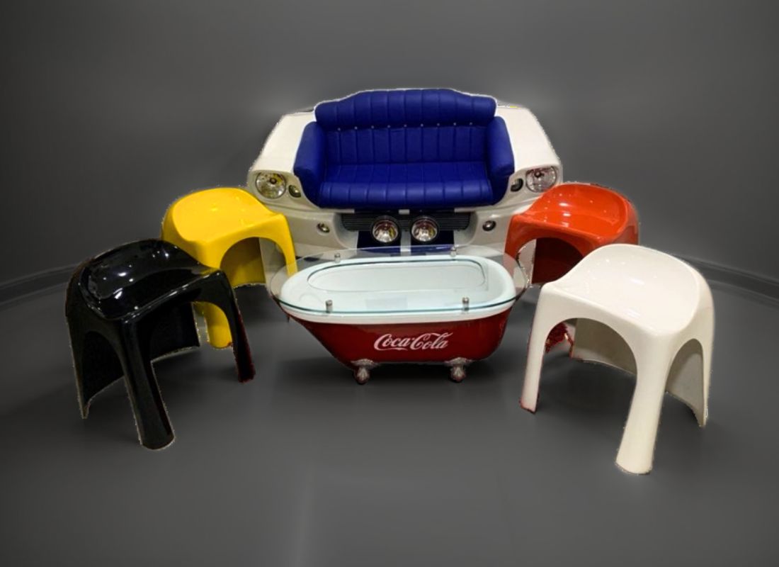 Conjunto com sofá azul sobre a frente branca de um carro clássico, mesa de centro vermelha Coca-Cola com tampo de vidro e bancos amarelo, vermelho, preto e branco
