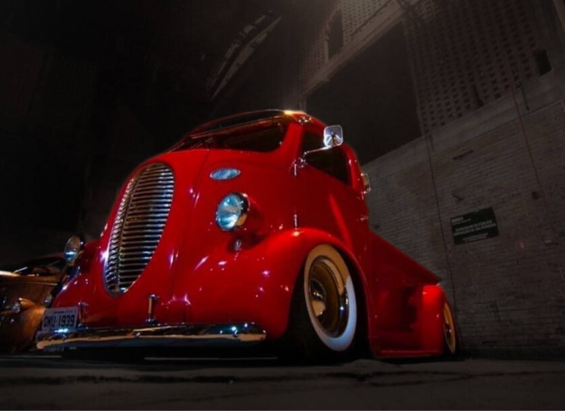 Ford COE 1939 vermelho personalizado, com pintura brilhante, grade cromada e pneus de faixa branca, fotografado à noite em um beco