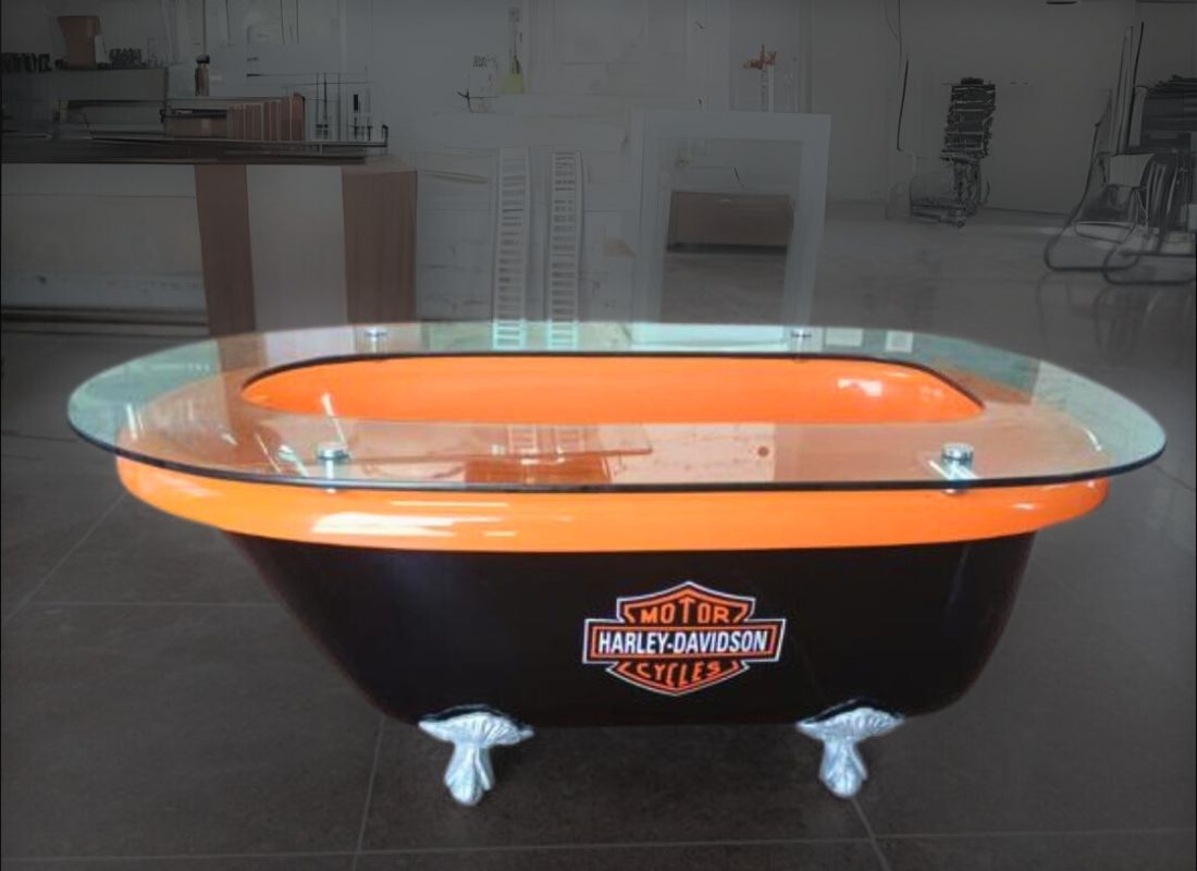 Mesa de centro feita de banheira antiga em fibra de vidro, laranja e preta, com pés prateados e tampo de vidro, com o emblema Harley-Davidson